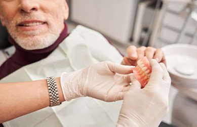 Dentist holding dentures while patient points to them