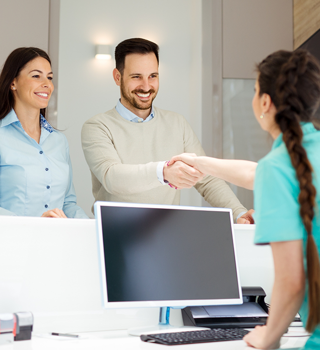 Dental team member shaking hands with a patient across a desk