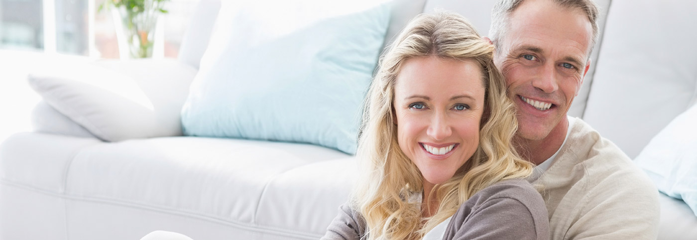 couple sitting in front of couch smiling brightly