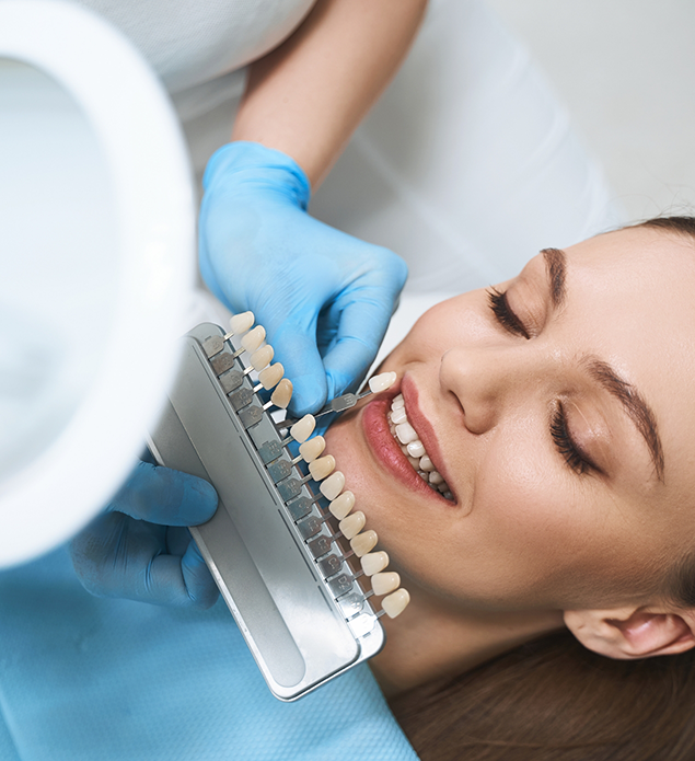 Dentist holding a veneer in front of a smiling patient's tooth