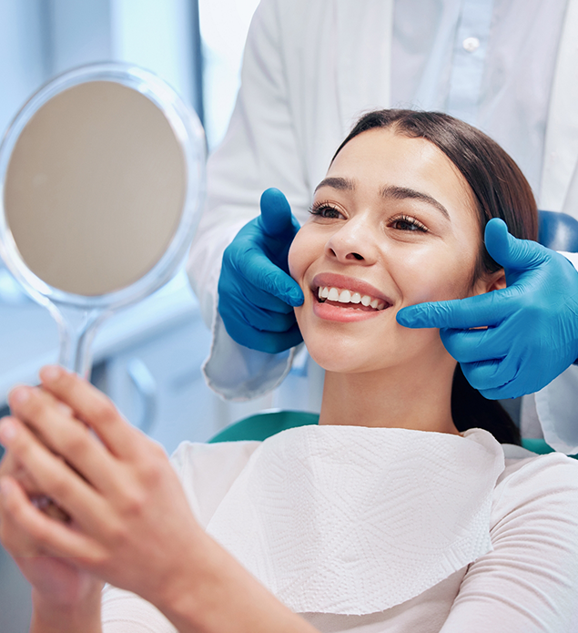 Young woman in the dental chair admiring her new smile in a mirror