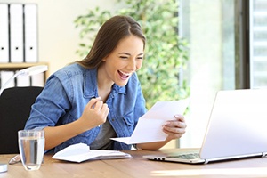 Woman celebrating at her desk because she saved money on dental care