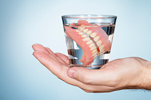 hand holding glass of water with dentures inside