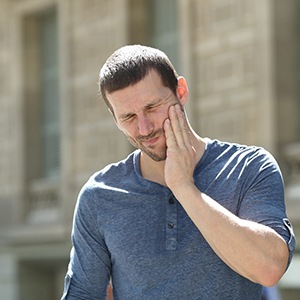 Man outside rubbing jaw due to failed dental implant in Sparks