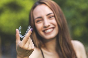 Woman holding aligner, enjoying benefits of SureSmile orthodontic treatment