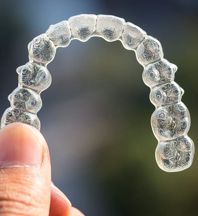 Close up of a hand holding a clear aligner