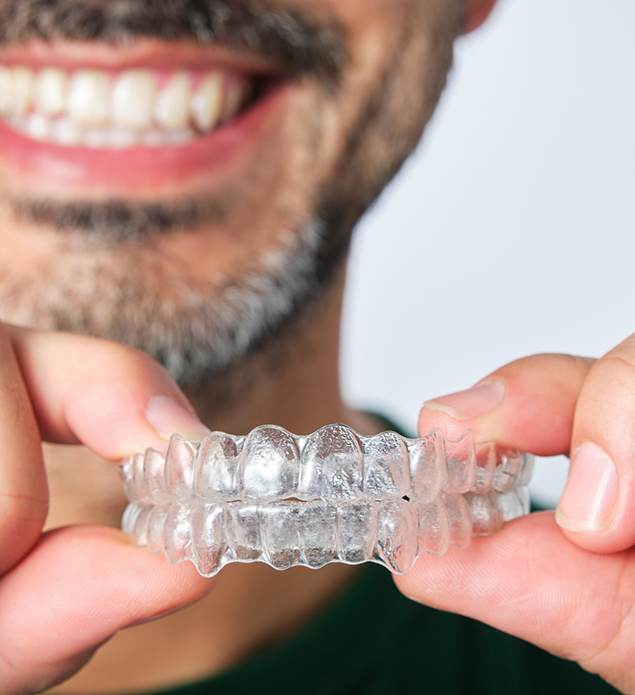 Smiling man holding two clear aligners