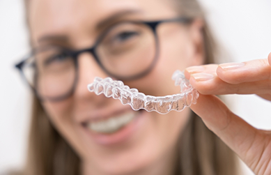Woman with glasses smiling and holding an aligner