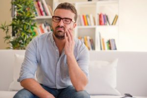 man who needs dental fillings holding his cheek in pain 