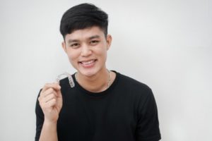 smiling man holding a SureSmile clear aligner