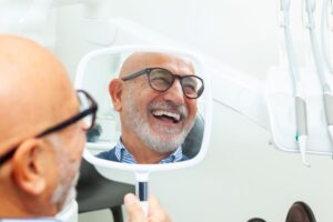 Smiling senior dental patient holding hand mirror