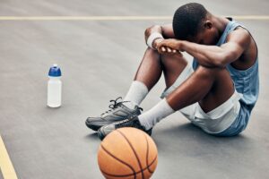 Young man sitting on ground with head hung down next to basketball and bottle of water