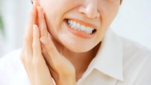 Woman wincing in pain and holding jaw (TMJ disorder).